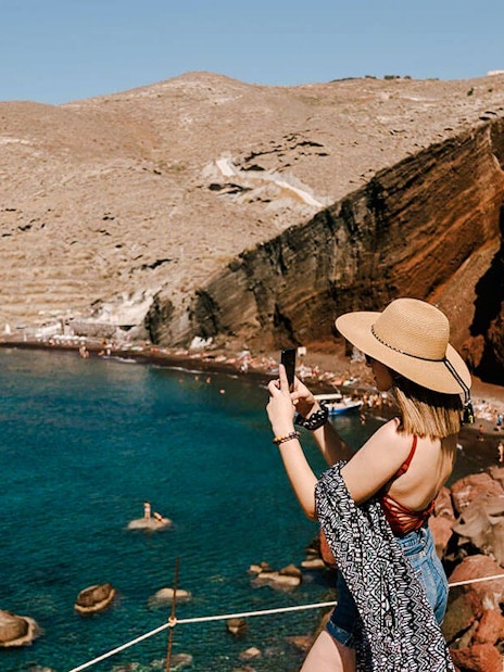 Woman photographing Red Beach cliffs in Santorini, Greece.
