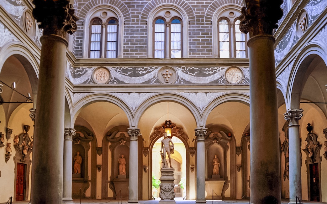 Palazzo Medici Riccardi courtyard with classical statues and ornate arches in Florence, Italy.