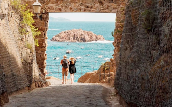 View through a stone archway in Vila Vella, Tossa de Mar, overlooking the sea and boats.