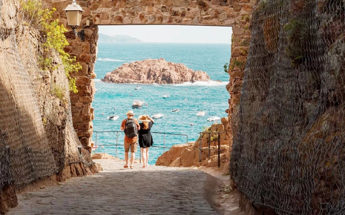 View through a stone archway in Vila Vella, Tossa de Mar, overlooking the sea and boats.