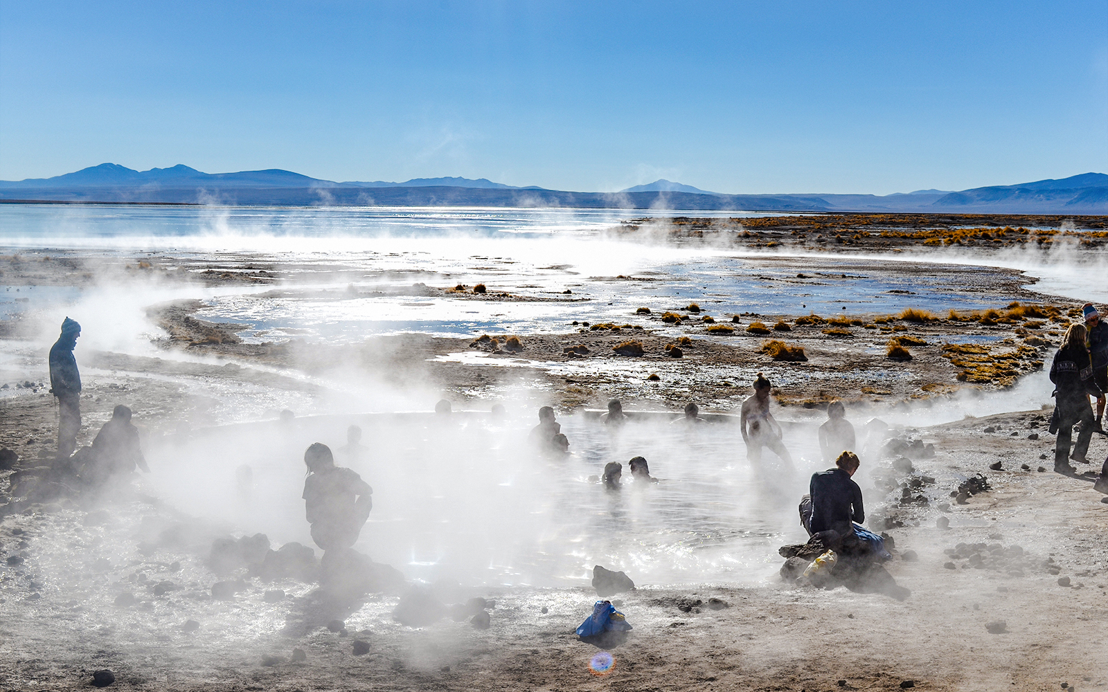 People enjoying Aguas Calientes hot springs with steam rising, surrounded by mountains.