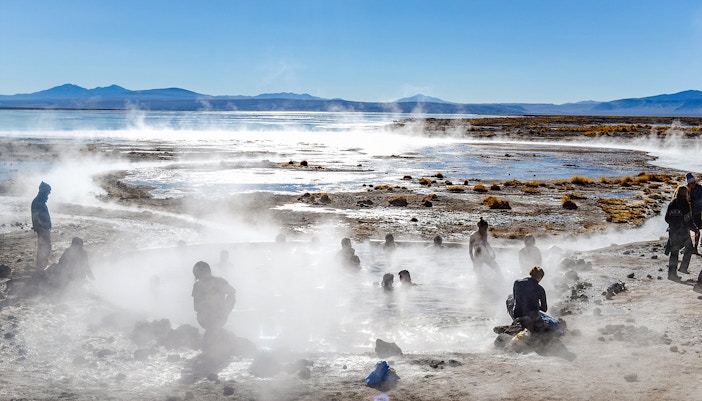 People enjoying Aguas Calientes hot springs with steam rising, surrounded by mountains.
