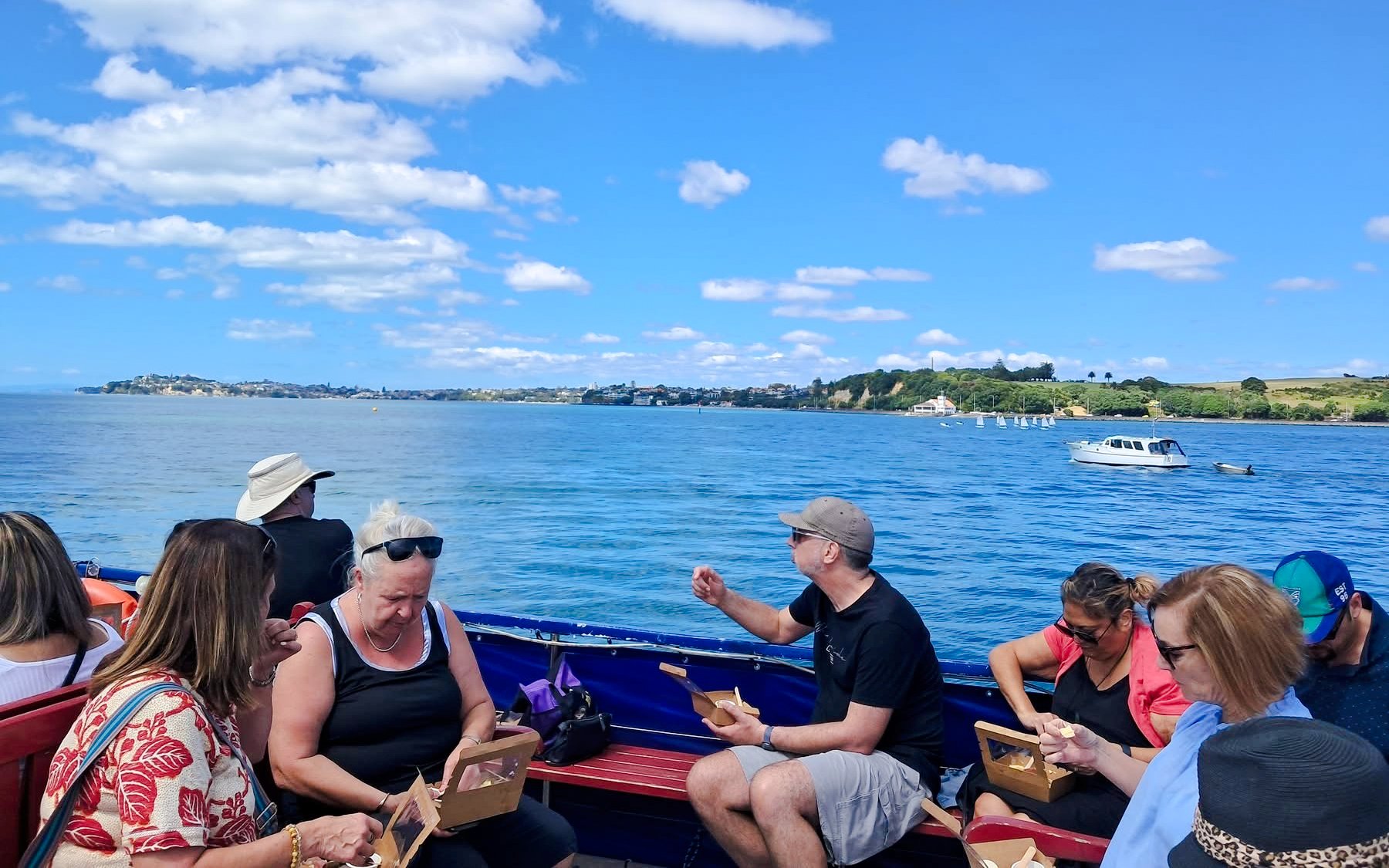 People enjoying wine and cheese on a harbour cruise with scenic coastal views.