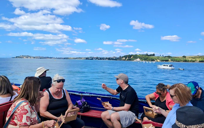 People enjoying wine and cheese on a harbour cruise with scenic coastal views.