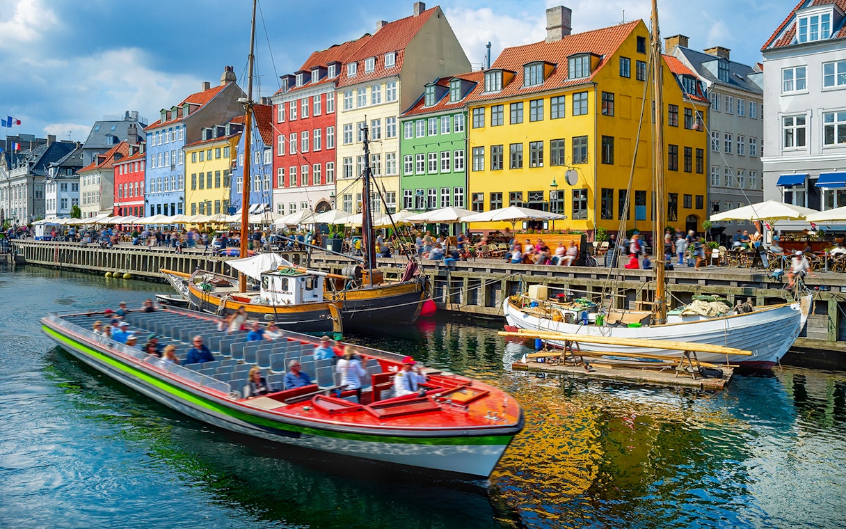 Tour boat cruising by colorful buildings in Nyhavn, Copenhagen.