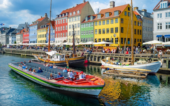 Tour boat cruising by colorful buildings in Nyhavn, Copenhagen.