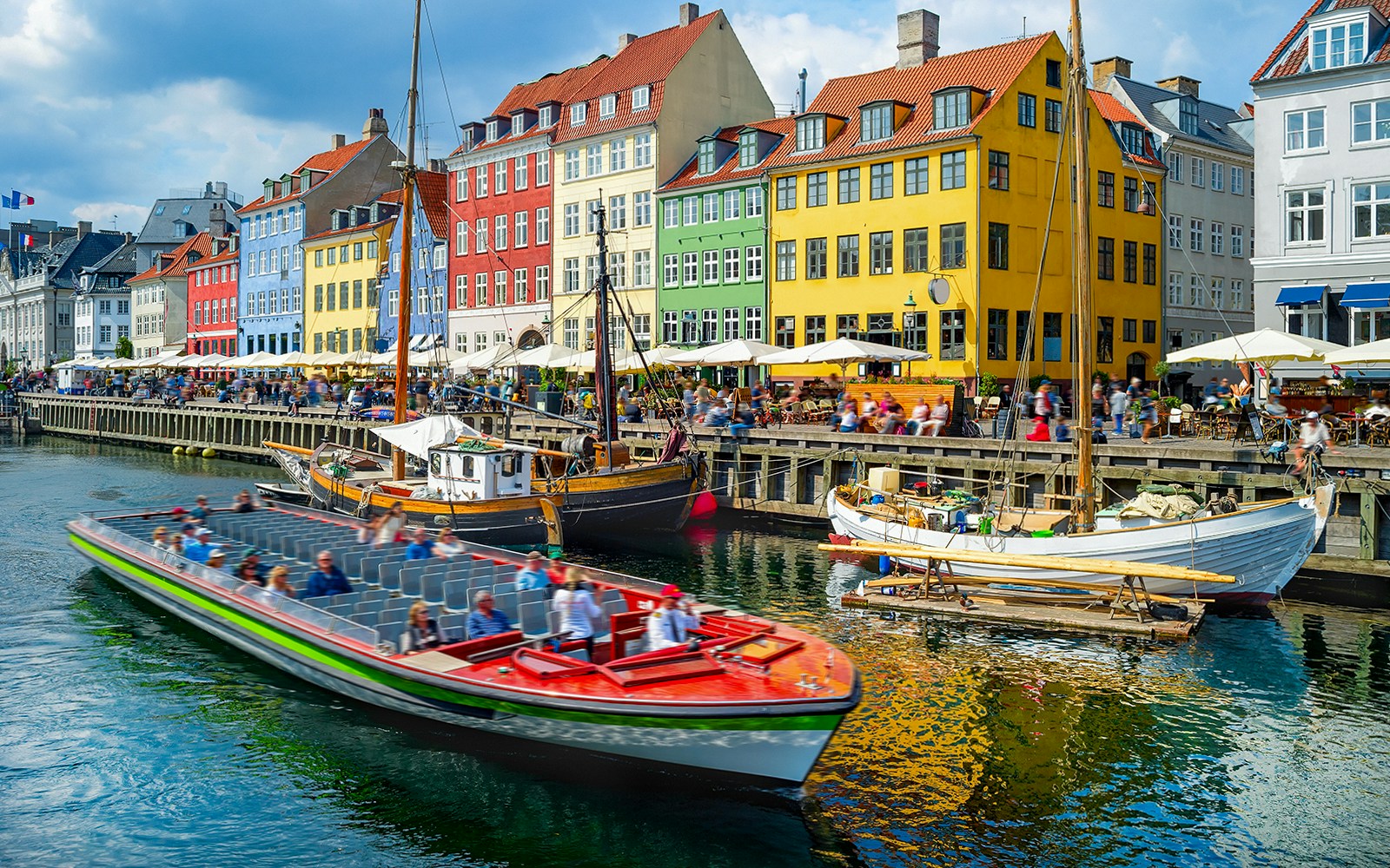 Touristic boat cruising by colorful buildings in Nyhavn, Copenhagen canal.