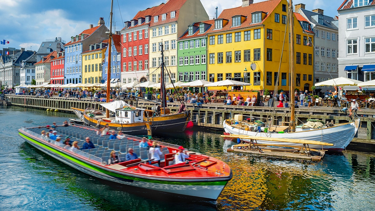 Touristic boat cruising by colorful buildings in Nyhavn, Copenhagen canal.