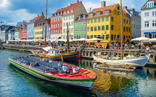 Tour boat cruising by colorful buildings in Nyhavn, Copenhagen.