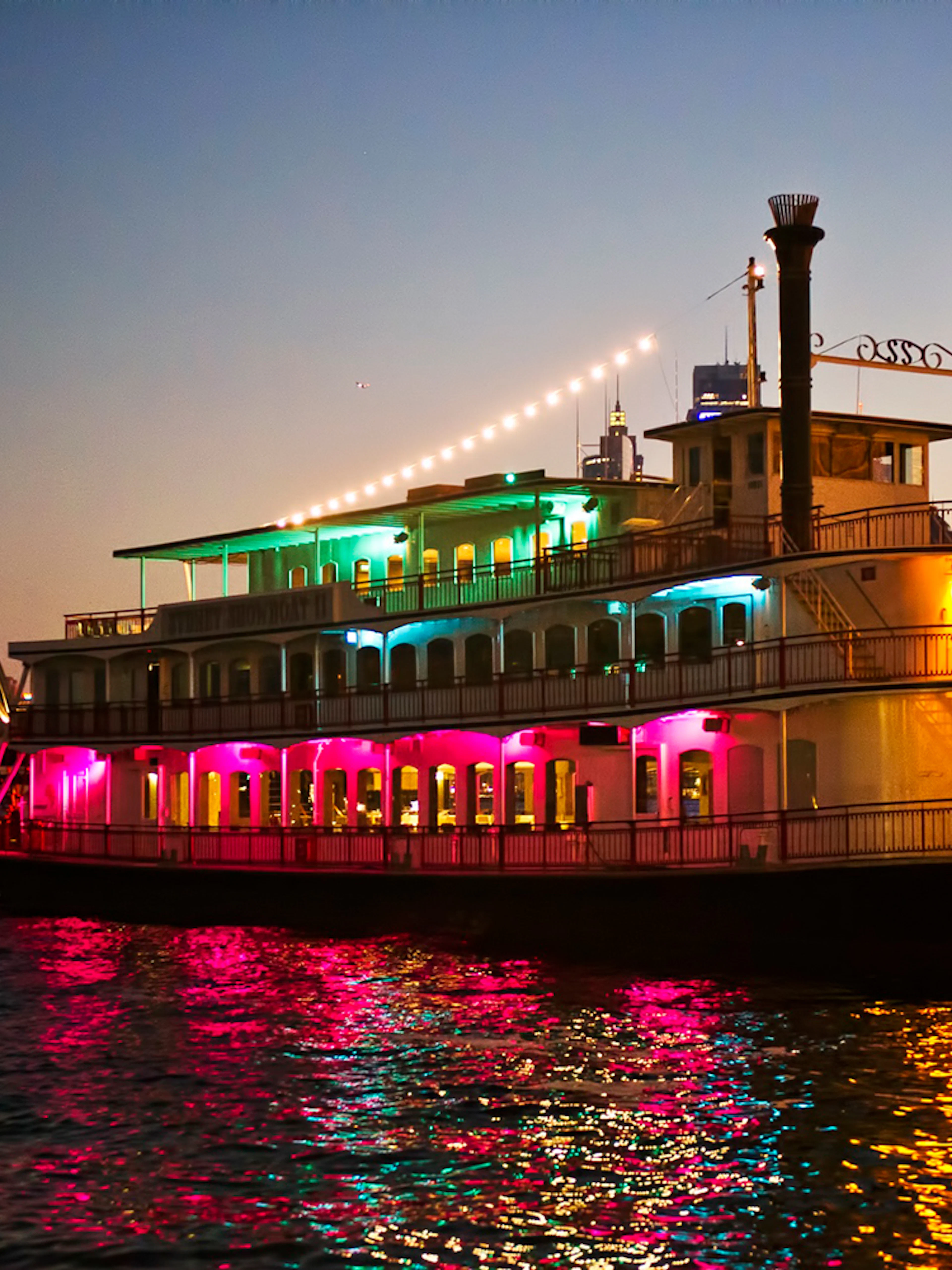 Cabaret cruise ship with colorful lights on Sydney Harbour near Opera House.