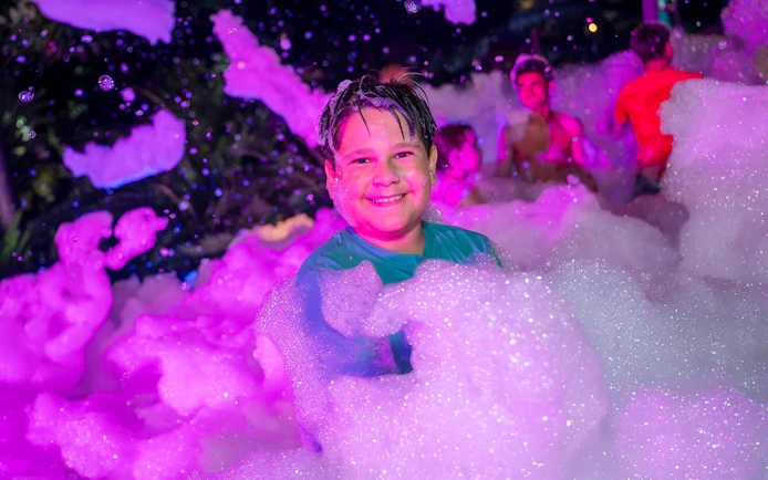 Child enjoying foam party at AquaGlow event, Aquatica San Antonio.