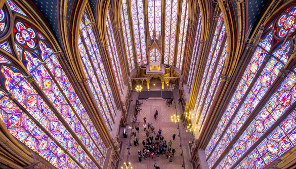 Group tour with guide inside Sainte Chapelle, Paris, viewing stained glass windows.