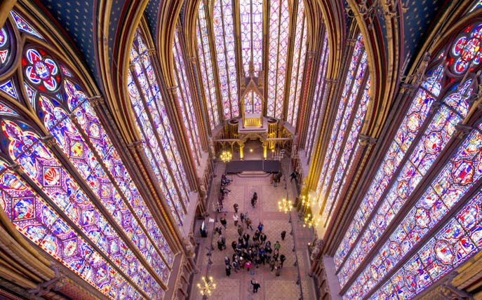 Group tour with guide inside Sainte Chapelle, Paris, viewing stained glass windows.