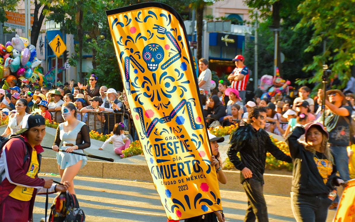 Day of the Dead parade in Mexico City with colorful banner and costumed participants.
