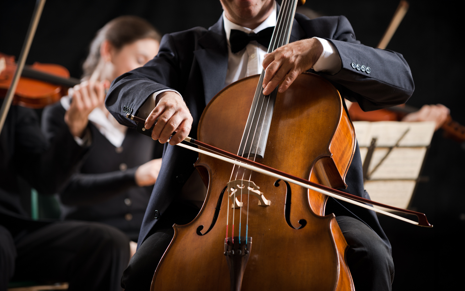 Cellist performing in a classical concert with orchestra in background.