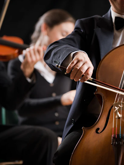 Cellist performing in a classical concert with orchestra in background.