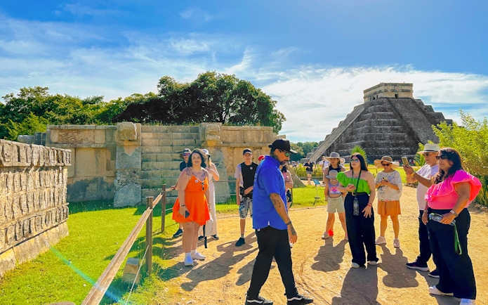 Tour guide explaining Chichen Itza temple and nearby ruins to a group of visitors.