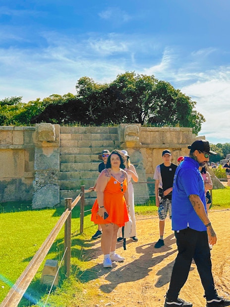 Tour guide explaining Chichen Itza temple and nearby ruins to a group of visitors.