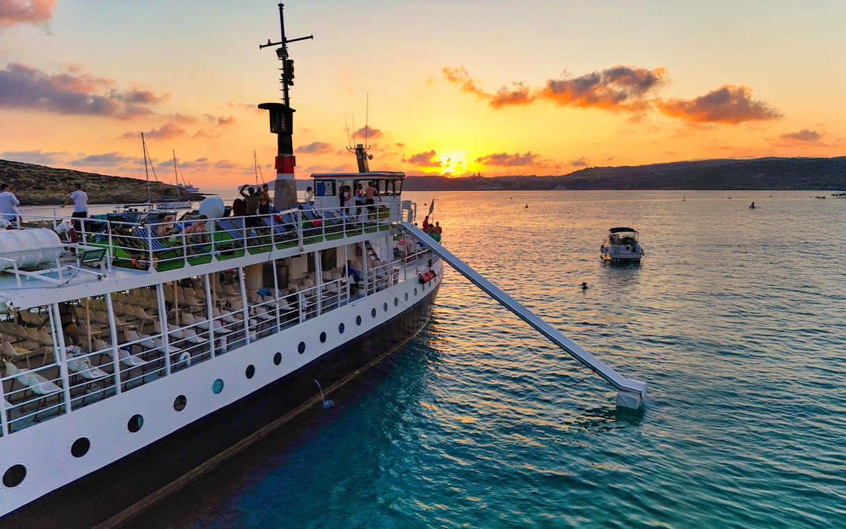 Cruise ship at sunset in Blue Lagoon, Malta, with passengers enjoying the view.