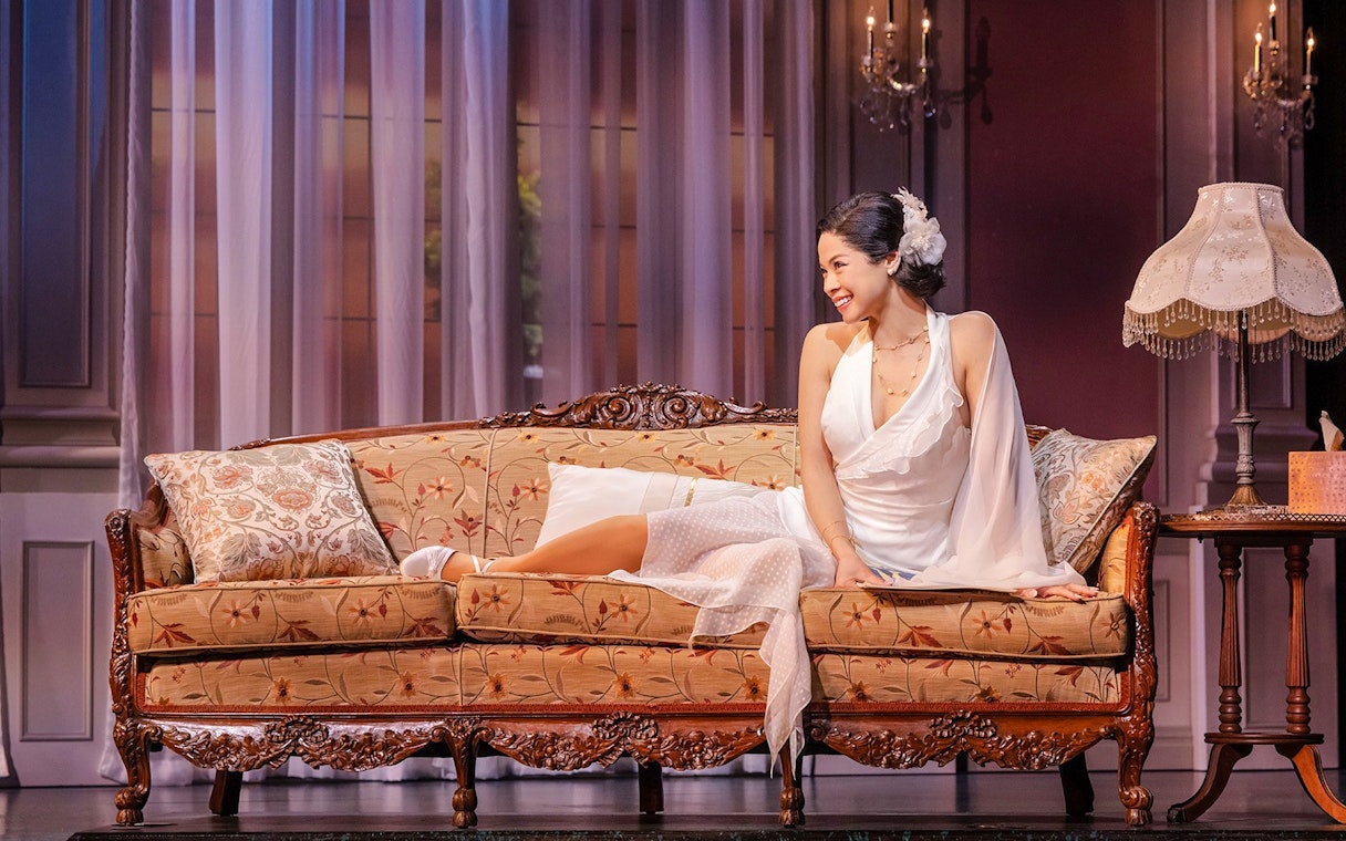 Stage scene from The Great Gatsby in New York with a woman on a vintage sofa.