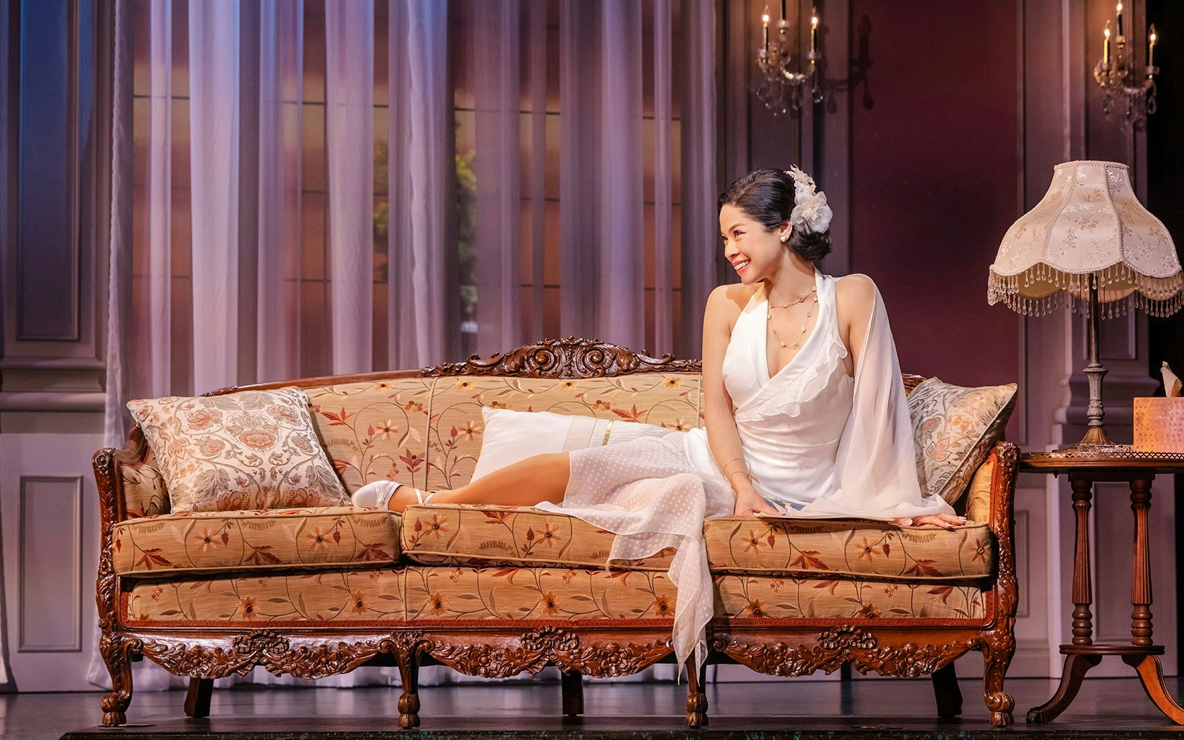 Stage scene from The Great Gatsby in New York with a woman on a vintage sofa.