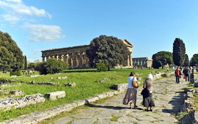 Visitors walking towards ancient Greek temples at Paestum Archaeological Park, Italy.