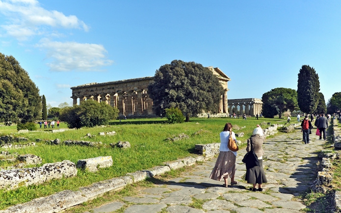 Visitors walking towards ancient Greek temples at Paestum Archaeological Park, Italy.