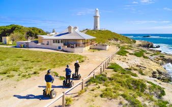 Segway riders on Rottnest Island near a coastal lighthouse.