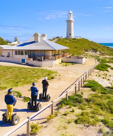 Segway riders on Rottnest Island near a coastal lighthouse.
