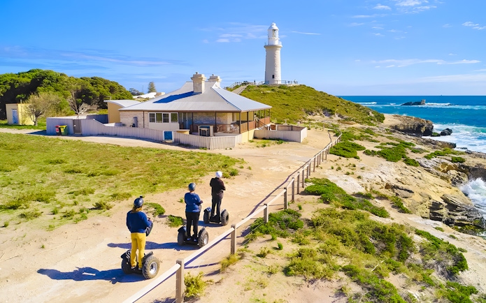 Segway riders on Rottnest Island near a coastal lighthouse.