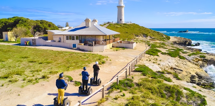 Segway riders on Rottnest Island near a coastal lighthouse.