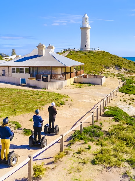 Segway riders on Rottnest Island near a coastal lighthouse.