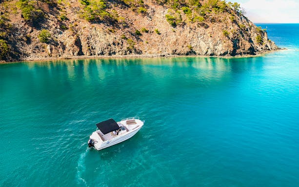 Speedboat cruising near rocky southern island coast with clear blue water.