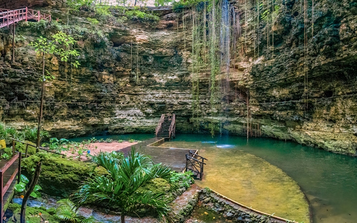 Chichikan cenote with wooden stairs and lush greenery in Valladolid, Yucatan, Mexico.