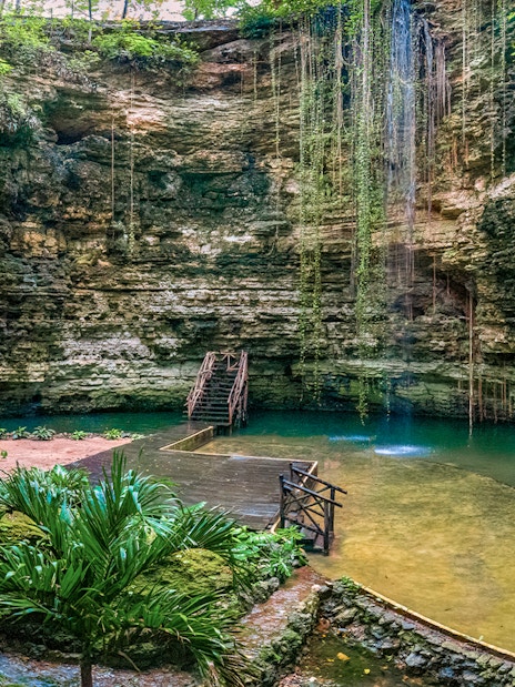 Chichikan cenote with wooden stairs and lush greenery in Valladolid, Yucatan, Mexico.