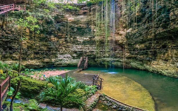 Chichikan cenote with wooden stairs and lush greenery in Valladolid, Yucatan, Mexico.