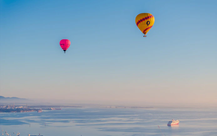 Hot air balloons over Geelong's coastal landscape, Australia, with a ship in the bay.