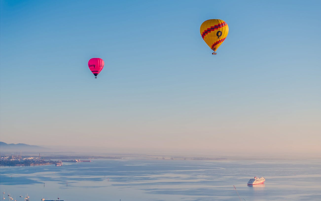 Hot air balloons over Geelong's coastal landscape, Australia, with a ship in the bay.