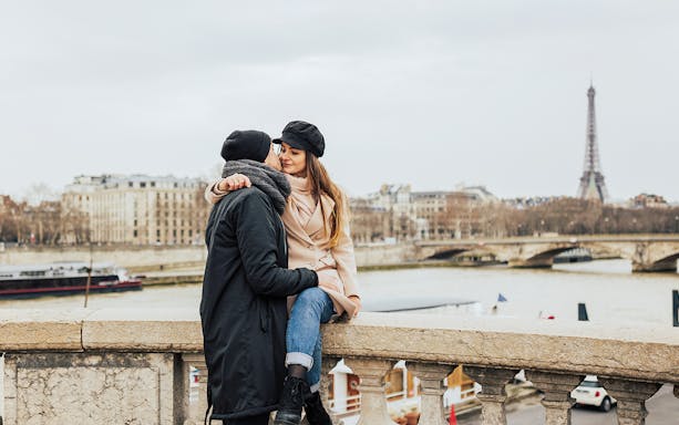 Couple embracing on a Parisian bridge with Eiffel Tower in the background.