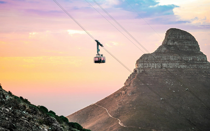 Aerial cable car ascending Table Mountain at sunset with Lion's Head in the background, Cape Town.