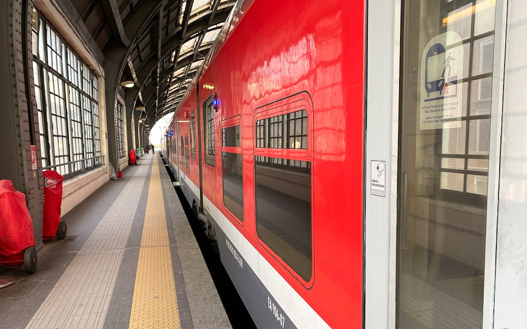 Red train at Milan Central Station platform for Malpensa Airport route.