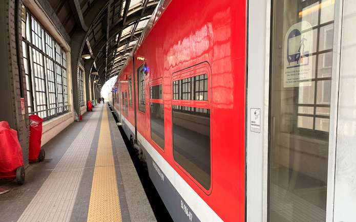 Red train at Milan Central Station platform for Malpensa Airport route.