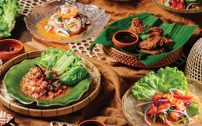 Thai food spread with shrimp salad, fried chicken, and spicy papaya salad at Akara Sky.