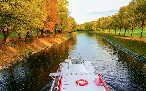 Cruise boat on Djurgrden City Canal surrounded by autumn trees.
