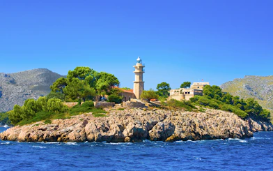 Lighthouse on rocky island with greenery, seen during catamaran trip in Alcudia.