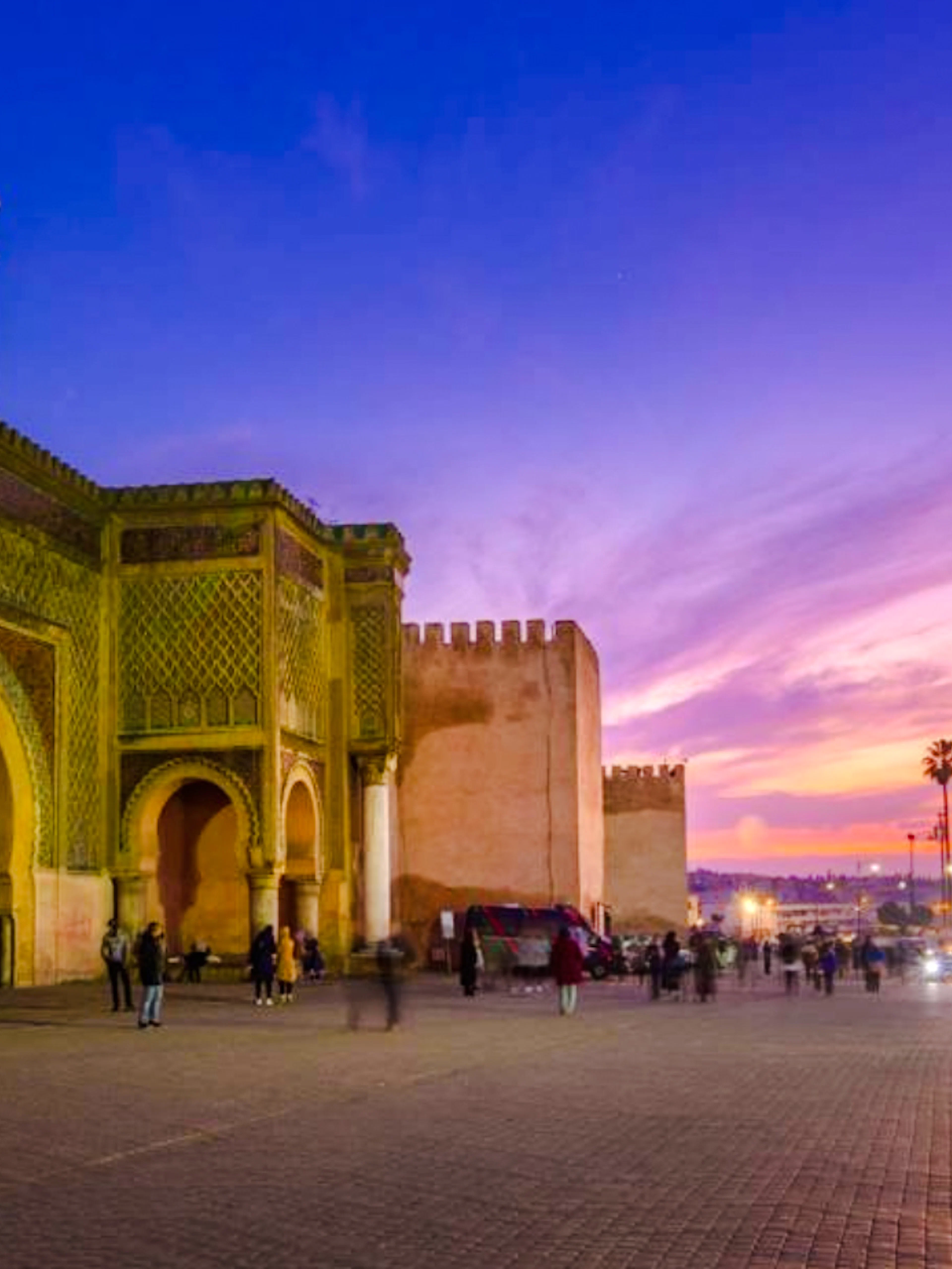 Bab Mansour gate in Meknes at sunset, with people and cars passing by.