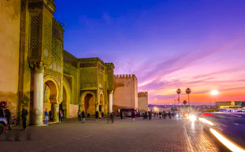 Bab Mansour gate in Meknes at sunset, with people and cars passing by.