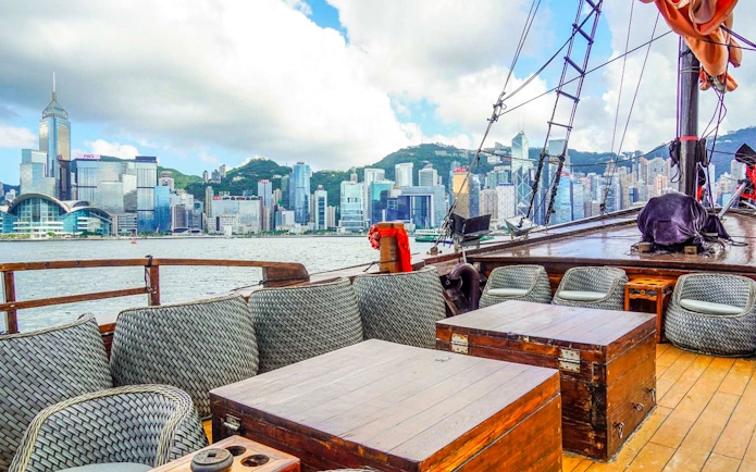 AquaLuna cruise deck with seating, overlooking Victoria Harbour and Hong Kong skyline.