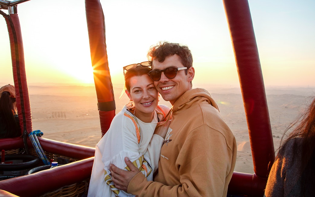 Couple enjoying sunrise during hot air balloon ride in Ras Al Khaimah desert.