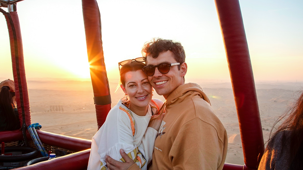 Couple enjoying sunrise during hot air balloon ride in Ras Al Khaimah desert.